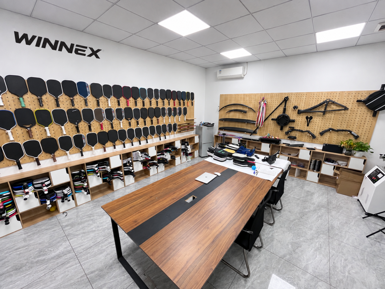 Inside the WINNEX pickleball paddle showroom: a wall of paddle samples, grip options and a sample review table